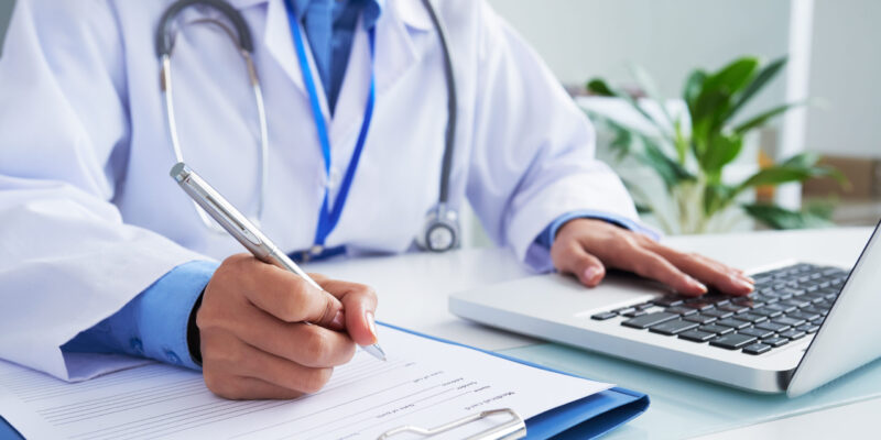 Doctor checking information in computer program before filling medical card