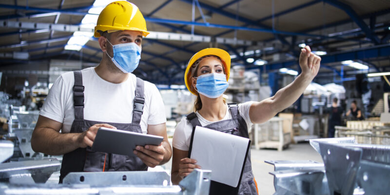 Factory workers with face masks protected against corona virus doing quality control of production in factory.